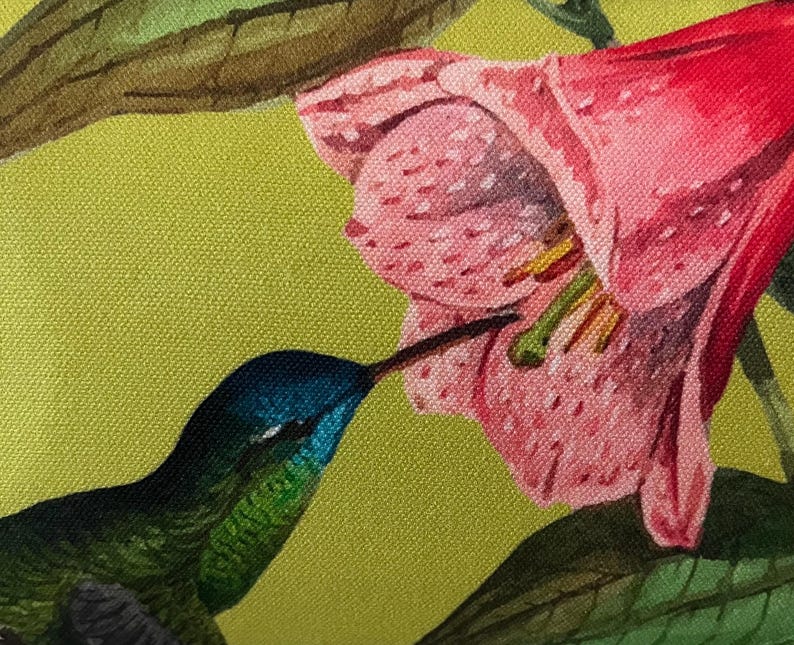 May include: A close-up of a vibrant textile print featuring a hummingbird and a pink flower. The hummingbird has a blue head and green body, with a long beak reaching into the flower. The background is a light green color.