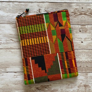 May include: A colorful zippered pouch with a geometric pattern in shades of red, yellow, green, and black. The pouch is made of fabric and has a drawstring closure.