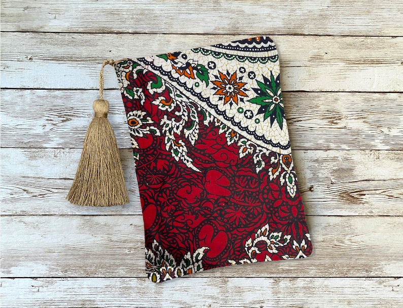 May include: A rectangular, patterned fabric pouch with a decorative tassel. The pouch features a red and white floral design with green and orange accents. The tassel is a light brown color.