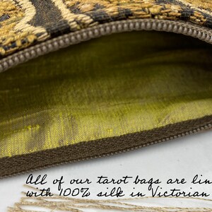 May include: Close-up of a tarot bag with a brown zipper and a gold and black patterned exterior. The interior is lined with Victorian gold silk. The text in the image reads: "All of our tarot bags are lined with 100% silk in Victorian gold."