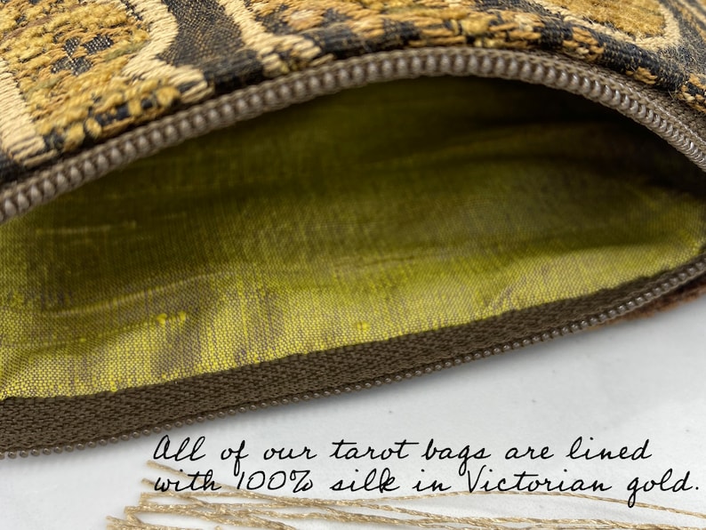 May include: Close-up of a tarot bag with a brown zipper and a gold and black patterned exterior. The interior is lined with Victorian gold silk. The text in the image reads: "All of our tarot bags are lined with 100% silk in Victorian gold."