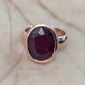 Könnte beinhalten: Ein Ring aus Roségold mit einem großen, ovalen, dunkelroten Edelstein.