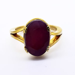 Könnte beinhalten: Ein goldener Ring mit einem großen, ovalen, dunkelroten Edelstein.