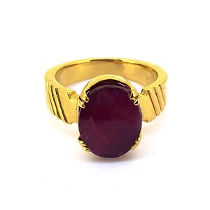 May include: A gold ring featuring a large, oval-shaped, dark red gemstone set in the centre. The ring band has a textured design.