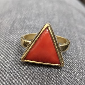Op de afbeelding: Een gouden ring met een driehoekige rode koraal edelsteen.