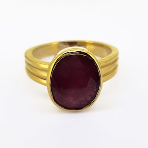 May include: A gold ring with a large, oval-shaped, dark red gemstone.