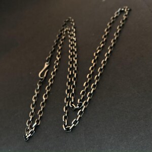 Könnte beinhalten: Eine silberne Kettenkette mit einem Hakenverschluss. Die Kette besteht aus kleinen, miteinander verbundenen ovalen Formen.