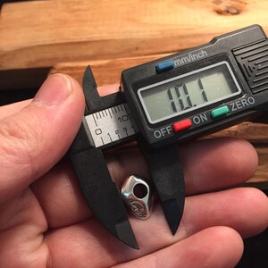 Op de afbeelding: Een zilveren bedel met een gedetailleerd ontwerp, gemeten met een digitale schuifmaat op 11,1 mm.