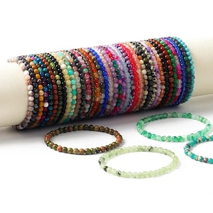 Puede incluir: Una colección de pulseras de piedras preciosas de colores, cada una con un patrón y una combinación de colores diferentes. Las pulseras están hechas de pequeñas cuentas redondas y están apiladas juntas.