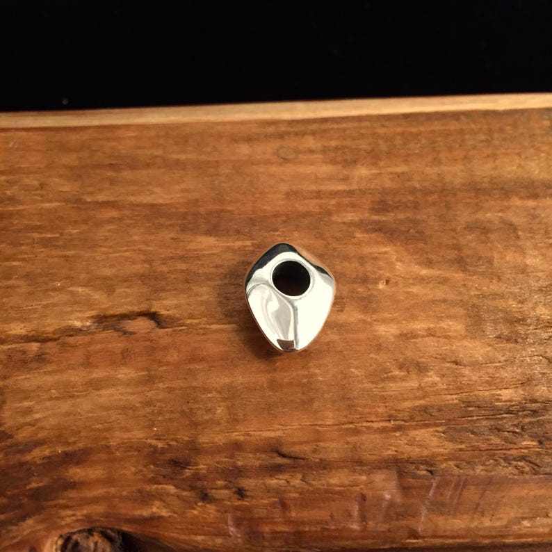 Op de afbeelding: Een zilveren hanger met een gladde, afgeronde, traanvormige vorm en een gat in het midden.