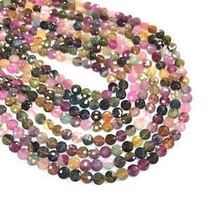 May include: A strand of multi-colored round gemstone beads. The beads are faceted and have a variety of colors, including pink, green, and brown. The beads are strung on a clear thread.