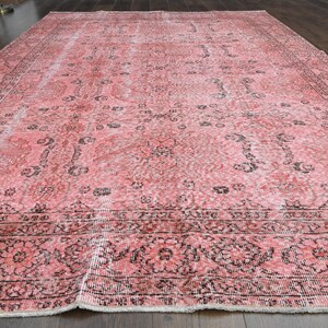 May include: A vintage pink and black patterned rug with a faded design. The rug has a fringed edge and is made of a soft, woven material.