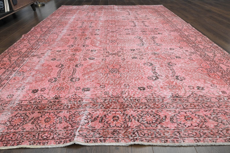 May include: A vintage pink and black patterned rug with a faded design. The rug has a fringed edge and is made of a soft, woven material.