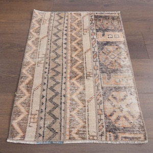 May include: A beige and brown patterned rug with a geometric design. The rug has a fringed edge and is made of a soft, woven material.