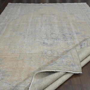 May include: A light gray rug with a faded blue pattern. The rug is folded in half and lying on a wooden floor.
