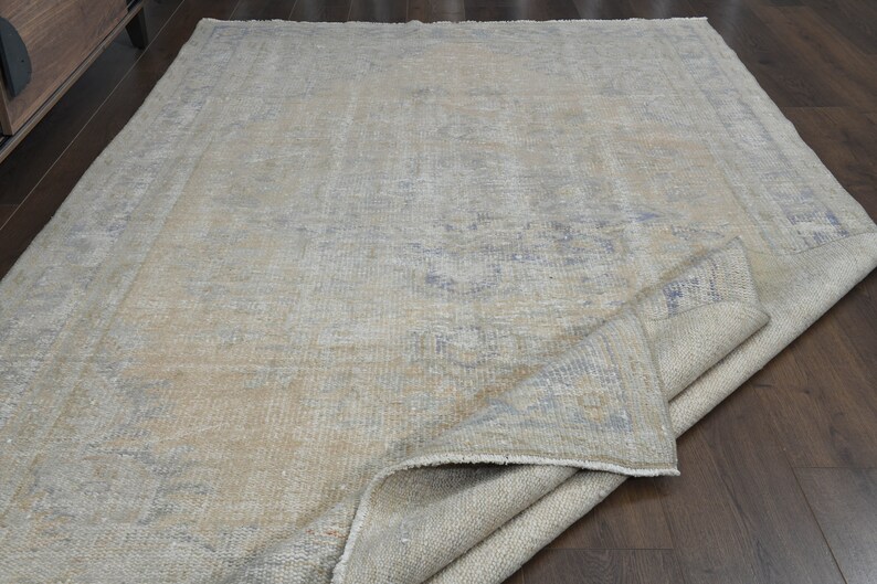 May include: A light gray rug with a faded blue pattern. The rug is folded in half and lying on a wooden floor.