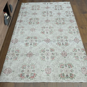 Puede incluir: Una alfombra blanca con un patrón floral en tonos rojos, verdes y rosas. La alfombra tiene un aspecto desgastado, lo que le da un toque vintage.