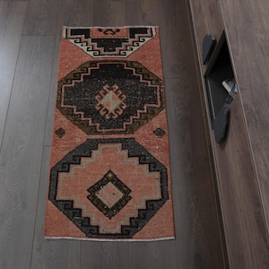 May include: A pink and black patterned rug with a geometric design. The rug is made of wool and has a fringed edge.