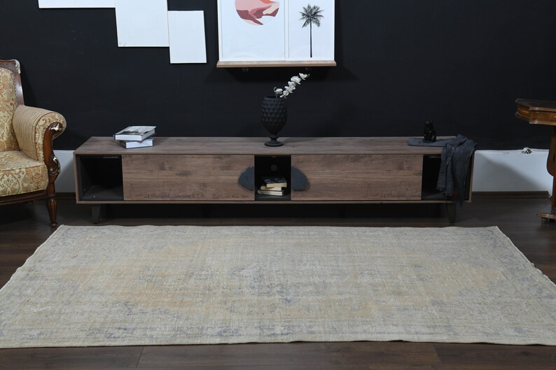 May include: A light beige rug with a faded floral pattern. The rug is placed in front of a wooden entertainment center with black metal legs. The entertainment center has two drawers and an open shelf.