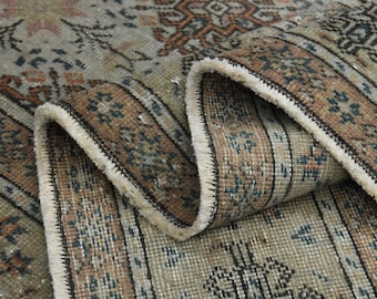 May include: Close-up of a rug with a detailed pattern in shades of brown, blue, and white. The rug has a fringe border and is folded in half.