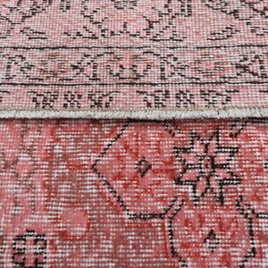 May include: A vintage pink and black rug with a geometric pattern. The rug has a fringe border.