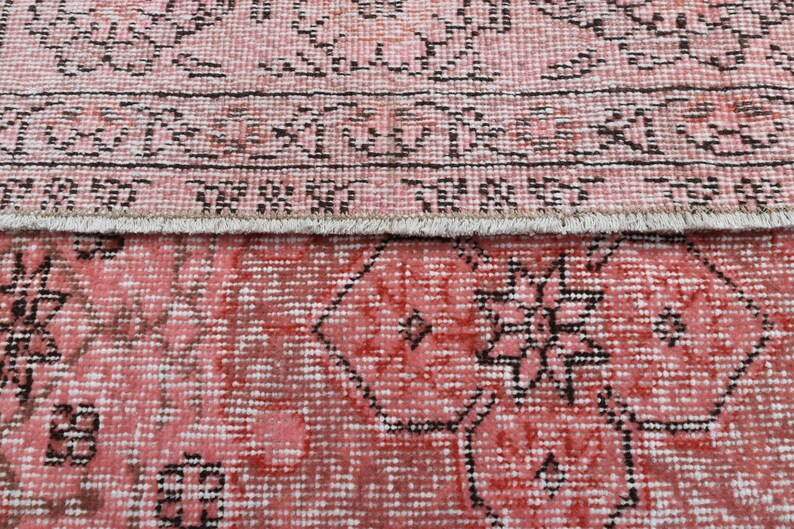 May include: A vintage pink and black rug with a geometric pattern. The rug has a fringe border.