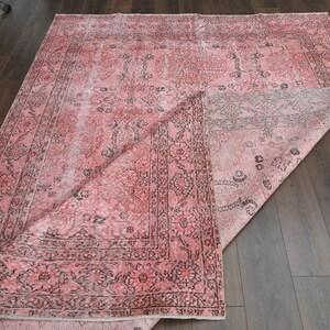May include: A pink and black vintage rug with a floral pattern. The rug is folded in half and lying on a wooden floor.