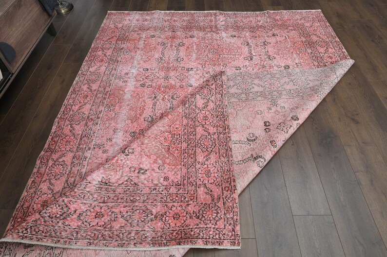 May include: A pink and black vintage rug with a floral pattern. The rug is folded in half and lying on a wooden floor.