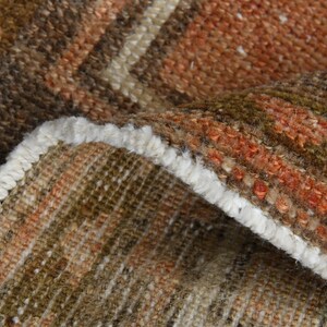 Könnte beinhalten: Nahaufnahme eines gewebten Teppichs mit weißem Fransen. Der Teppich hat eine braune, orange und beige Farbgebung.