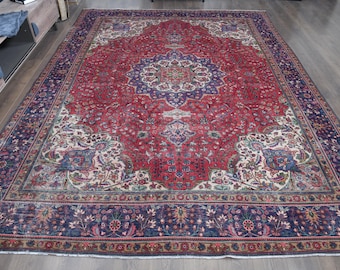 May include: A large rectangular area rug featuring a deep red central field with a prominent blue and cream floral medallion. The rug is framed by a wide dark blue border filled with intricate floral patterns in shades of pink, green, and tan.