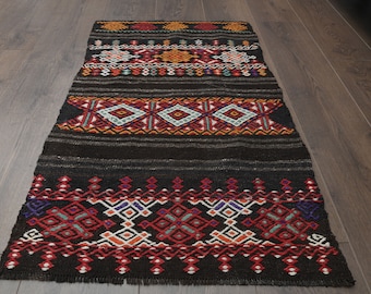 May include: A black and red patterned rug with geometric designs. The rug has a fringe border and is made of wool.