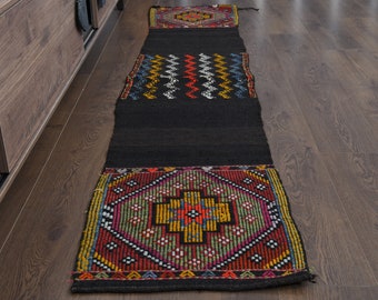 May include: A black and colorful patterned rug with geometric designs. The rug has a black background with red, yellow, green, blue, and white accents. The rug is made of wool and has a traditional design.