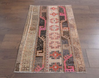 May include: Rectangular, vintage-style rug with a patchwork design. The rug features vertical stripes in beige, brown, black, and pink, with geometric patterns. The rug is placed on a dark brown wooden floor.