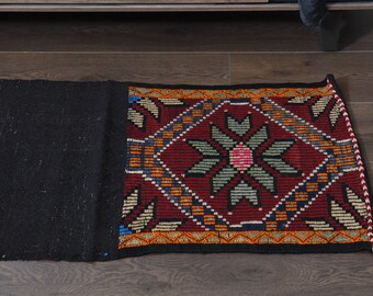 May include: A black and red patterned rug with a geometric design. The rug has a fringe border and is made of wool.