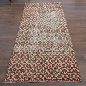 May include: A red, brown, and white patterned runner rug with a geometric design. The rug is made of a soft, woven material and has a fringed edge.