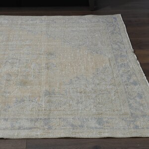 May include: A light beige rug with a faded blue floral pattern and a border. The rug has a distressed look and is made of a soft, woven material.