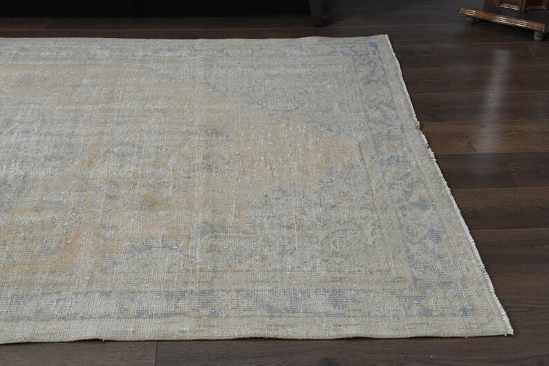 May include: A light beige rug with a faded blue floral pattern and a border. The rug has a distressed look and is made of a soft, woven material.