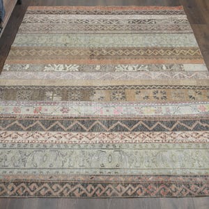 Puede incluir: Una alfombra de estilo vintage con un patrón a rayas en tonos marrones, beige y grises. La alfombra tiene un aspecto desgastado y presenta intrincados diseños geométricos.