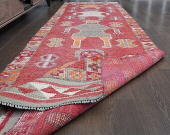 May include: A red, orange, and gray patterned runner rug with a geometric design. The rug is folded in half and lying on a dark wood floor.
