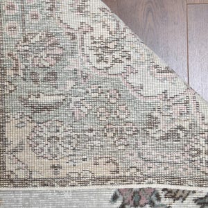 May include: Close-up of a beige rug with a floral pattern. The rug has a woven texture and a faded appearance.