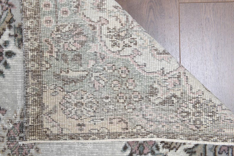 May include: Close-up of a beige rug with a floral pattern. The rug has a woven texture and a faded appearance.