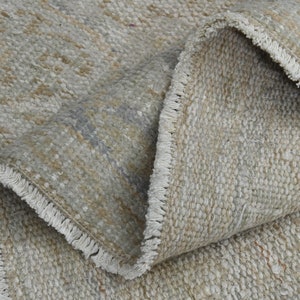 May include: Close-up of a beige and gray woven rug with a fringe border. The rug is folded in half, showing the texture of the weave.