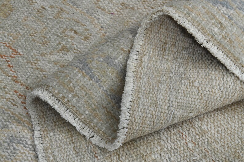 May include: Close-up of a beige and gray woven rug with a fringe border. The rug is folded in half, showing the texture of the weave.