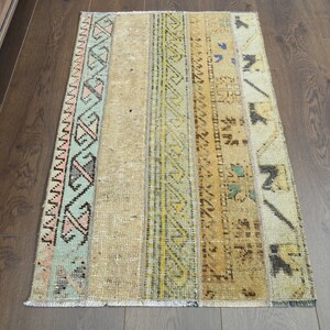 May include: A vintage style rug with a beige background and colorful geometric patterns in shades of pink, blue, green, and yellow. The rug has a frayed edge and is made of woven fabric.