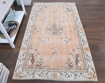May include: A vintage-style rug with a peach background and a floral pattern. The rug has a cream-colored border with a geometric design.