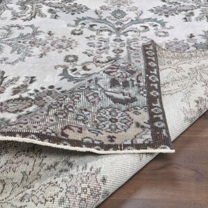 May include: A close-up of a rug with a floral pattern in shades of brown, gray, and white. The rug is folded in half, showing the underside of the fabric.
