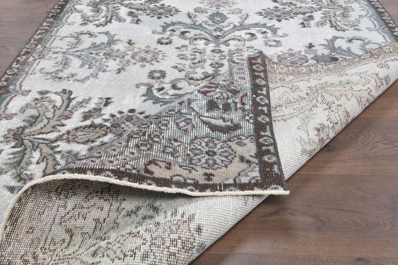 May include: A close-up of a rug with a floral pattern in shades of brown, gray, and white. The rug is folded in half, showing the underside of the fabric.