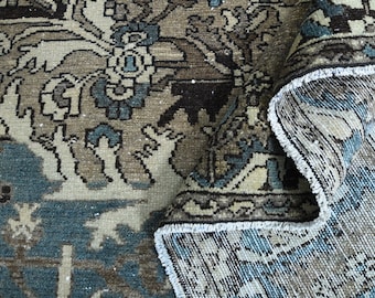 May include: An antique rug with a distressed, vintage look. The rug features a complex floral pattern in shades of blue, beige, and brown. The edges are frayed, adding to the rug's aged appearance. The rug is partially rolled up, revealing the underside.