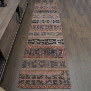May include: A long, narrow rug with a colourful geometric pattern in shades of red, orange, blue, and black. The rug has a distressed, vintage look and is perfect for adding a touch of bohemian style to any room.