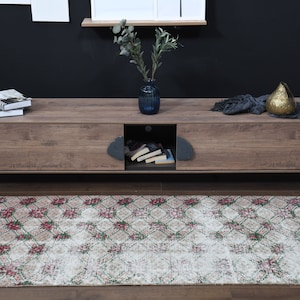 May include: A wooden TV stand with two sliding doors and a shelf. The stand has black metal legs and is decorated with a vase of greenery and a throw blanket. A patterned rug is in front of the stand.